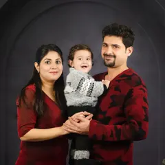 A warm family portrait with a smiling baby held between his parents. The coordinated red and grey sweaters are perfect for this cozy, fine-art style.
