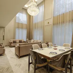 The dining area flows seamlessly from the living space, unified by a consistent palette and grand proportions. Sheer curtains soften the light, creating an elegant atmosphere for any occasion.