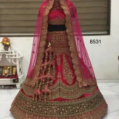A mannequin display of a classic rani pink bridal lehenga. This piece features heavy gold zardozi work and traditional kalire, showcasing a quintessential North Indian bridal style.