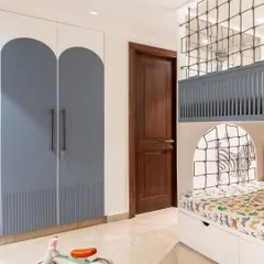 The wardrobe doors feature a playful arched design in blue, tying into the room's color scheme. The space is designed to be clutter-free, with plenty of room for play.