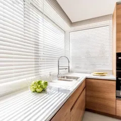 Clean, white Venetian blinds are a perfect choice for this modern kitchen. They are easy to clean, moisture-resistant, and allow for precise control of light over the countertop.