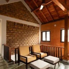 The family room in the Basavanagudi 'Thotti mane' combines exposed handmade adobe brick masonry with a warm, orange-toned Lohi plaster. The vaulted wooden ceiling and traditional pillar add to the cozy, rustic ambiance.