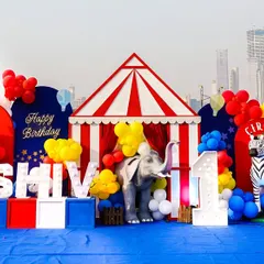 A grand circus-themed birthday setup against a city skyline, complete with a big top tent, animal props, and marquee letters spelling out the birthday boy's name.