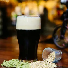 This shot showcases a dark stout or porter. The focus is on the rich color of the beer and its creamy head, with the pub's warm, ambient lighting creating a cozy, inviting mood.