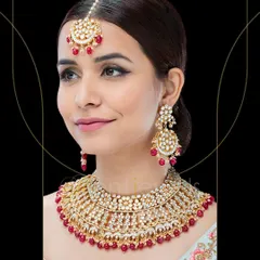 Accessorize your wedding outfit with this gorgeously crafted Polki Kundan bridal necklace set. The red beads add a traditional pop of color, and the set includes a matching maang tika.