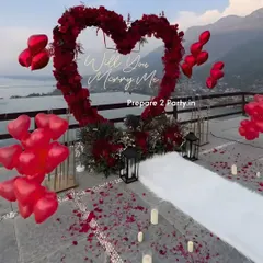 Leveraging a stunning natural view, this terrace proposal features a large heart-shaped arch made of deep red flowers. A white aisle runner, scattered petals, LED candles, and heart-shaped balloons create a clear path for a memorable walk-up to the big question.
