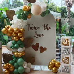 A beautiful setup for a baby shower celebrating twins, with the message 'Twice the Love'. The decor uses an arched backdrop and a sophisticated balloon garland in sage green, white, and chrome gold.