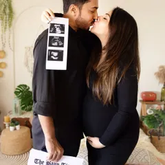 A classic pregnancy announcement photo. The couple holds up their ultrasound pictures and a custom "Baby Times" newspaper.