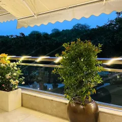 As evening approaches, fairy lights along the railing add a magical glow to this balcony garden, highlighting the beautiful plants and the retractable awning.