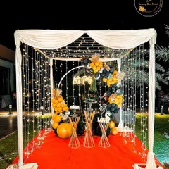 We can create a stunning focal point for any party. This "Let's Party" setup includes a cabana draped with fabric and fairy lights, a neon sign, and a black and yellow balloon arrangement.