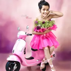 A fun and stylish shot of a ten year old girl in a unique pink dress made of flowers, posing on a matching pink toy scooter. This shows a creative concept for older kids' photoshoots.