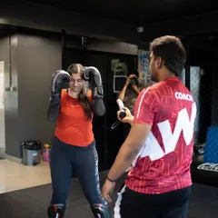 A coach gives one-on-one instruction to a female fighter, correcting her guard and stance. Personalized feedback is key to improvement.