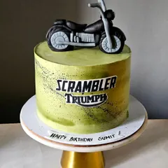 A cool and stylish cake for a motorcycle enthusiast. This design features a lime green airbrushed cake with a "Scrambler Triumph" logo and a detailed, hand-sculpted edible motorcycle on top.