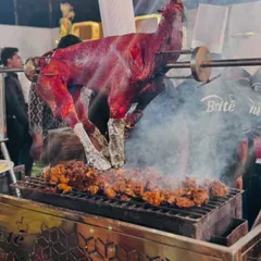 A close-up of the whole roasted mutton, showing the rich color and texture as it cooks over hot coals.