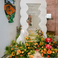 A personalized welcome mirror with a modern wavy frame, surrounded by sunflowers, tropical leaves, and quirky animal and mushroom props.