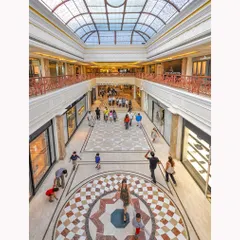 A high-angle shot of the mall's interior, emphasizing the intricate floor patterns, glass ceiling, and the movement of shoppers. This perspective highlights the architectural volume and design.