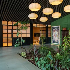 An indoor garden runs through the center of the sales lounge, bringing life and fresh air into the space. The open-slat ceiling and large globe pendant lights create a bright, airy atmosphere that promotes well-being for both staff and visitors.
