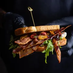 I hold up my signature BLT, a sandwich I'm truly proud of. It’s packed with crispy bacon, onion jam, and arugula, a combination that hits all the right notes.