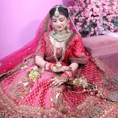 A beautiful bride seated in a magnificent pink and red dual-tone lehenga. This shot highlights the expansive flare of the skirt and the detailed craftsmanship of both the outfit and the matching emerald-accented bridal jewellery.