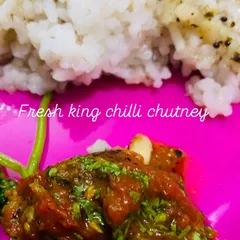 A spoonful of fresh king chilli chutney served with rice. The vibrant red colour and fresh green herbs show how fresh the ingredients are.