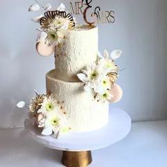My signature white wedding cake, a 3kg vision of sheer beauty and elegance. This two-tier Chocolate-Dulce de Leche cake features a textured finish and is adorned with fresh white flowers and macarons.