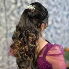 A close-up of a party hairstyle featuring a high ponytail with soft, cascading curls. The look is finished with a delicate pearl hair accessory for a touch of elegance.