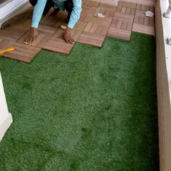 This image shows the installation process for a balcony floor. I am laying the interlocking wooden deck tiles directly onto the artificial grass base, a technique that creates a clean and professional finish.