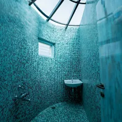 Curved geometry meets tactile design. This bathroom, lined with blue mosaic tiles and topped with a curved skylight, brings light, texture, and spatial drama together.
