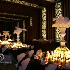 A glamorous anniversary celebration with a dramatic red and black theme. The room is filled with candlelit tables, large white feather centerpieces, and a stunning stage with a heart-shaped light installation.