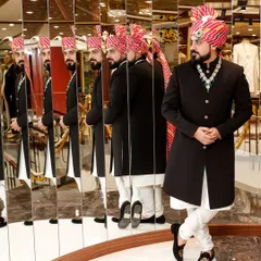 The mirror reflects your light, so shine on. Here, a client tries on a classic black Bandhgala in my store, surrounded by reflections that show the outfit from every angle.