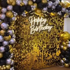 A close-up of a glamorous golden sequin wall with a 'Happy Birthday' neon sign, framed by black, silver, and gold balloons.