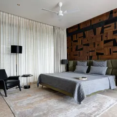 This bedroom in the Celadon residence features a unique accent wall made of reclaimed wood in a geometric pattern. We paired this rustic element with a modern olive green headboard, a classic black leather armchair, and soft, neutral textiles to create a balanced and tranquil space.