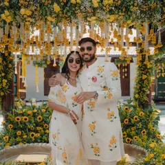 A happy couple poses in front of their stunning Haldi decor. Dressed in coordinated floral outfits, they are all smiles, surrounded by a sea of sunflowers and marigolds that perfectly match the joyous occasion.