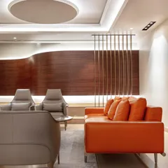 In the formal living room of the Wanderlust Villa, a bold orange sofa provides a vibrant contrast to the neutral tones and curved wood-paneled wall. The design is a balance of modern energy and timeless sophistication.