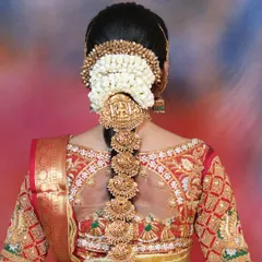 A close-up of a bridal jade bille with intricate temple designs and ruby stones. This is a must-have for a traditional South Indian bridal hairstyle.