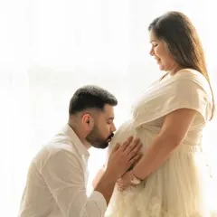A tender moment captured with soft, natural light from a window. The father-to-be kisses the baby bump, creating a simple yet powerful image of love and anticipation.