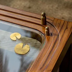 The beauty of our work is in the details. This close-up of our Kulam side table shows the custom-crafted brass elements that tell a story. Inspired by a tranquil Kerala temple pond, or 'kulam', these details depict lotus leaves and small figures, turning a simple table into a cherished memory.