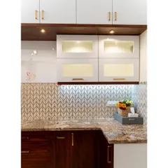 This kitchen in #TheRaghuvaniHome features a beautiful blend of white and wood-finish cabinets. The fluted glass shutters on the upper cabinets add a touch of elegance, while under-cabinet lighting illuminates the workspace.