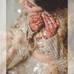 A detailed shot of the bride putting on her earrings. This close-up captures the intricate mehendi, the sparkling diamond ring, and the stunning details of her sequined and feathered lehenga.