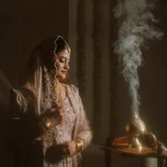 A bride stands amidst fragrant smoke from an incense burner, a traditional element in many cultures. The dramatic lighting creates a serene and almost spiritual portrait before her Nikkah.