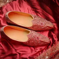 A close-up of the groom's traditional shoes (juttis) on a rich, red fabric.