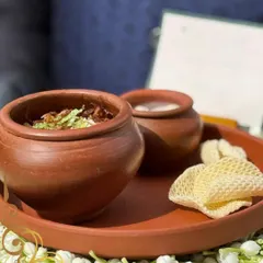 Our soul-stirring Dum Biryani, slow-cooked in a traditional terracotta pot and served with raita and papad on a bed of fragrant jasmine flowers.