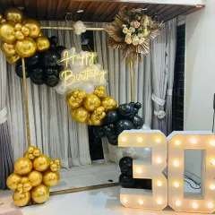 Celebrating a 30th birthday with style. This chic setup features a modern gold, black, and white balloon arrangement on a metal frame, a custom 'Happy Birthday' neon sign, and large marquee numbers, creating a sophisticated photo corner for the party.