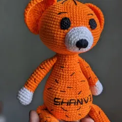 A bright orange tiger plushie, personalized with the name 'SHANVI' on its tummy. The black stripes are all hand-stitched.