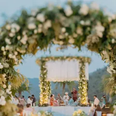 A dreamy perspective of our 'Luxe Garden' wedding mandap. The floral archway, filled with lush white roses and greenery, perfectly frames the ceremony space, creating a moment that feels like walking into a fairytale.
