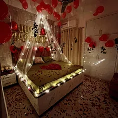 This wide-angle shot shows how the entire bedroom is transformed for a first night celebration. The combination of ceiling balloons, a lit canopy, and a floor covered in rose petals creates a complete romantic environment.