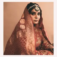 The bride's gaze, framed by a traditional bandhani dupatta. The rich red and gold tones of her outfit are a classic choice, styled here with a vintage aesthetic for a look that is both regal and deeply personal.