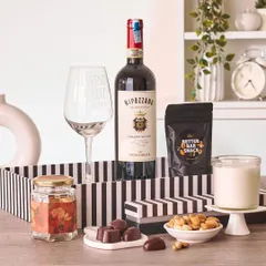 A beautifully styled wine and chocolate hamper, perfect for a cozy evening in. It features a bottle of Nipozzano, a "I wine a lot" glass, and assorted gourmet snacks.