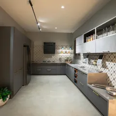 An L-shaped kitchen display in our Coimbatore showroom, featuring grey cabinets, a patterned tile backsplash, and integrated appliances for a clean, modern look.