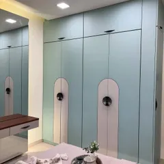 This custom wardrobe in a soft blue finish includes sleek, handleless doors and unique arched paneling, offering ample storage with a modern aesthetic.